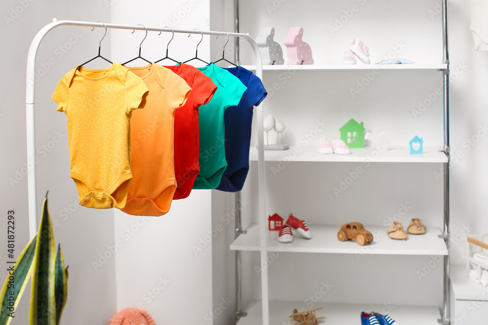 Rack with colorful baby bodysuits in light childrens room