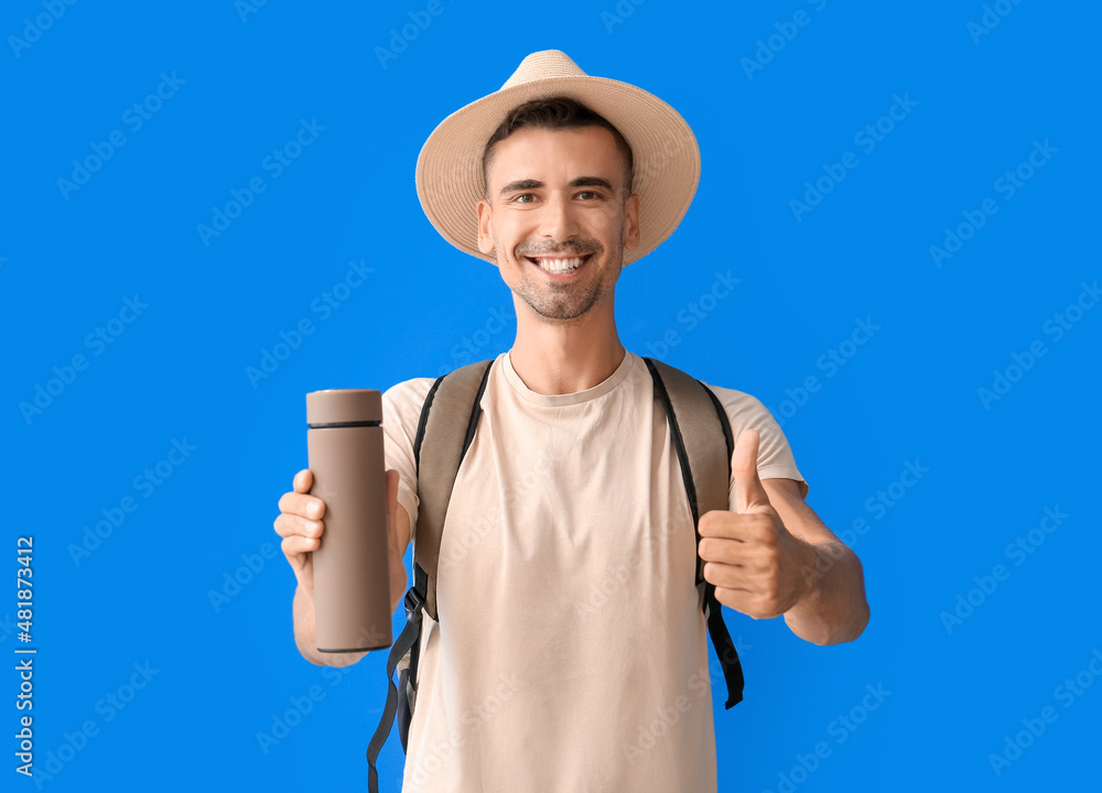 Male tourist with thermos showing thumb-up on color background