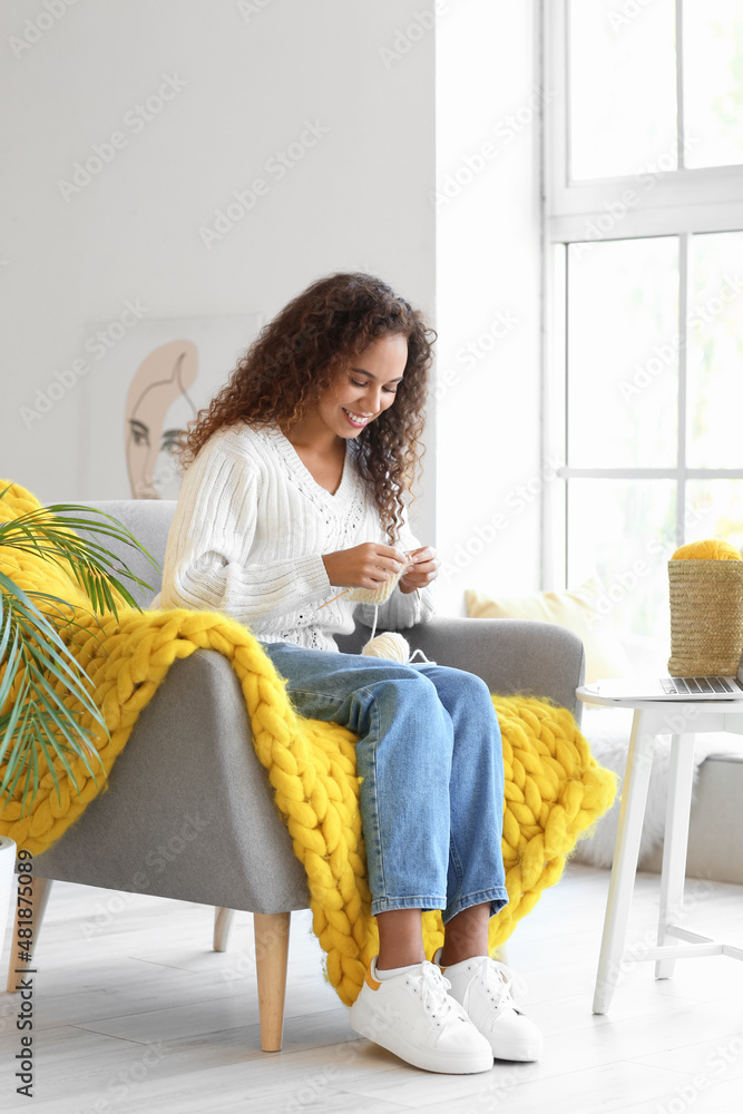 Young African-American woman taking online knitting classes at home