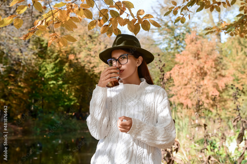 Beautiful young girl with hot drink near lake in park