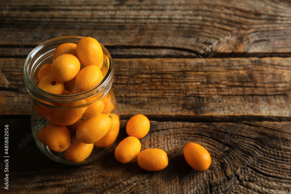 Jar with tasty kumquat fruits on wooden background