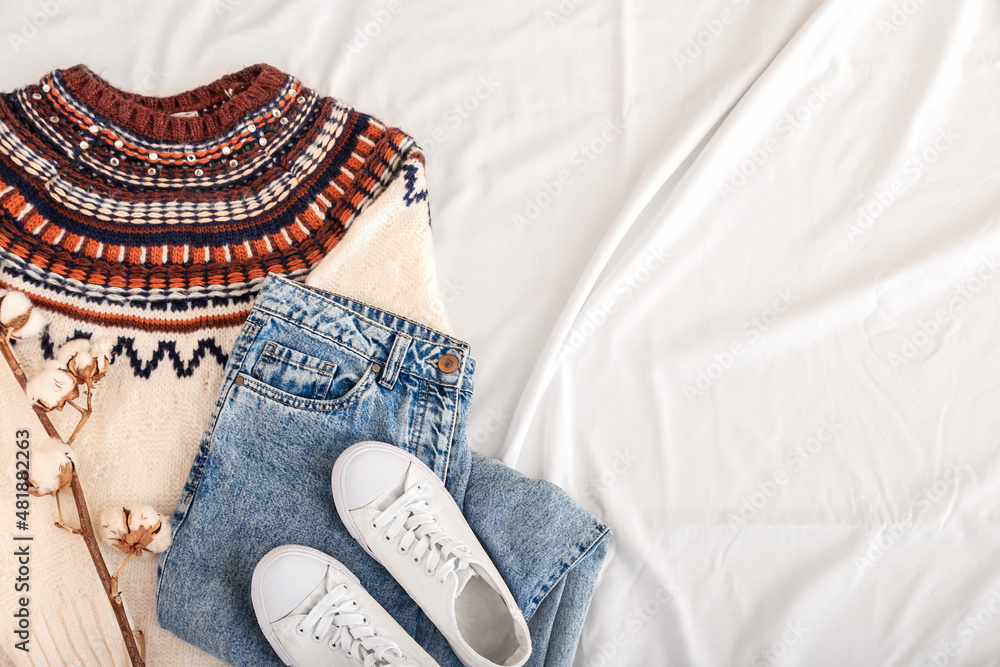 Stylish sweater, jeans, shoes and cotton flowers on light fabric background