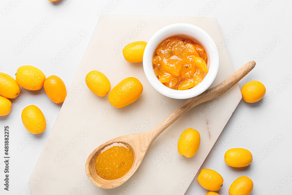 Bowl and spoon of tasty kumquat jam and fresh fruits on white background