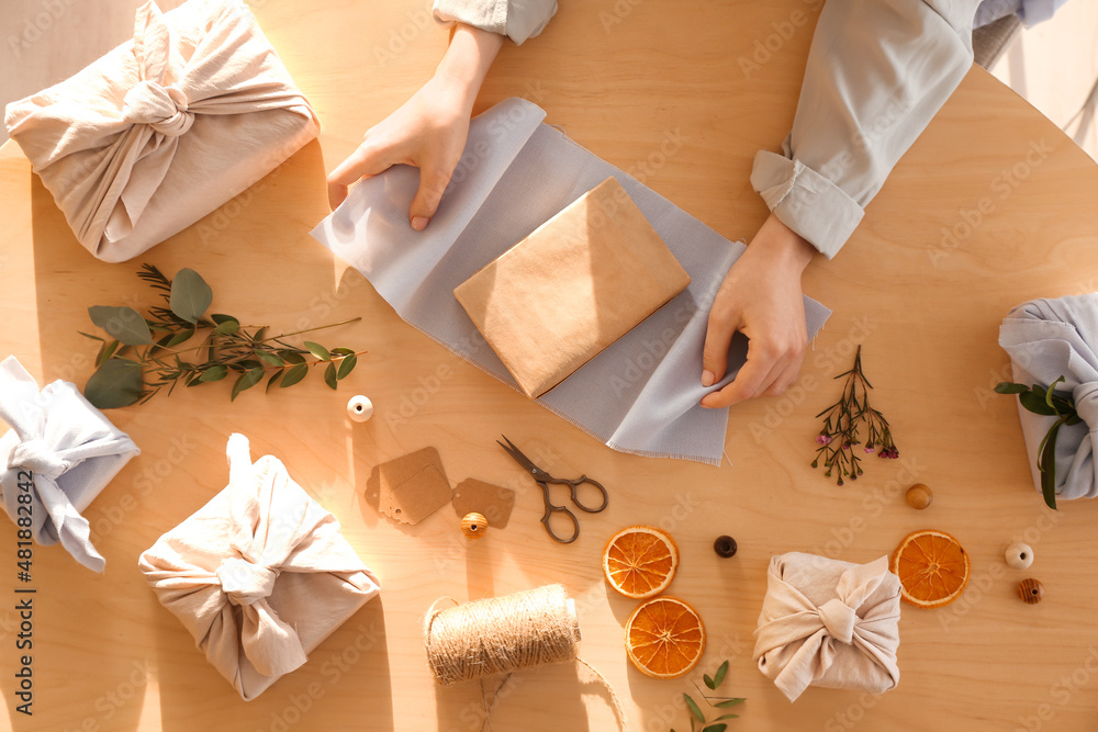 Woman wrapping gift box in fabric on wooden background