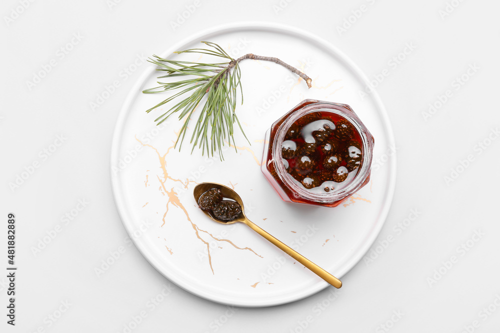 Plate with jar of tasty pine cone jam on light background