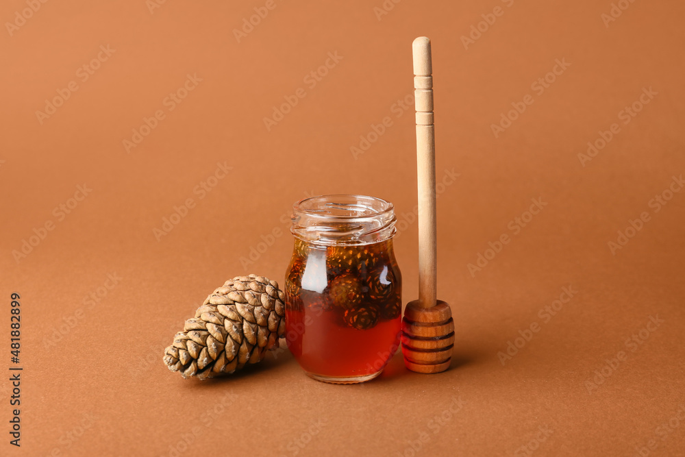 Jar of tasty pine cone jam and dipper on color background