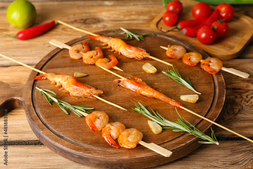 Board with grilled shrimp skewers on wooden background