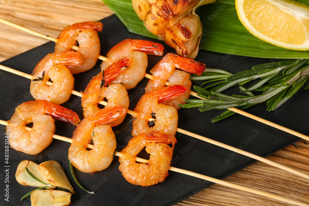 Board with grilled shrimp skewers on wooden background, closeup