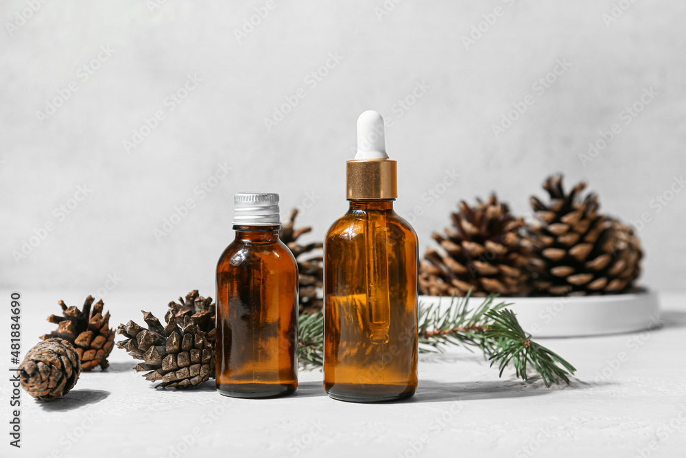 Bottles of essential oil and pine cones on light background