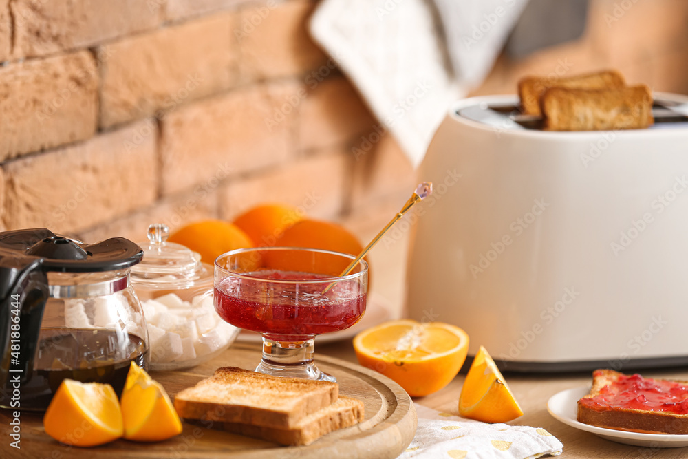 Glass bowl with jam, toasted bread and orange slices on counter in kitchen, closeup