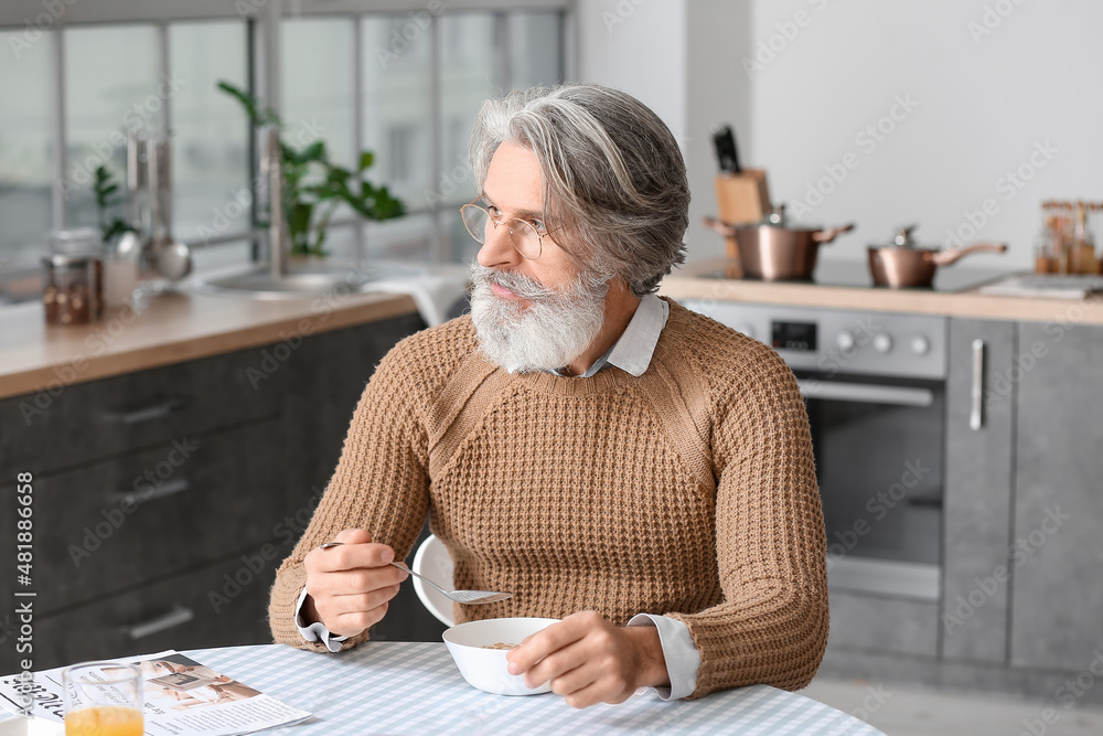 Senior man having breakfast at table in kitchen