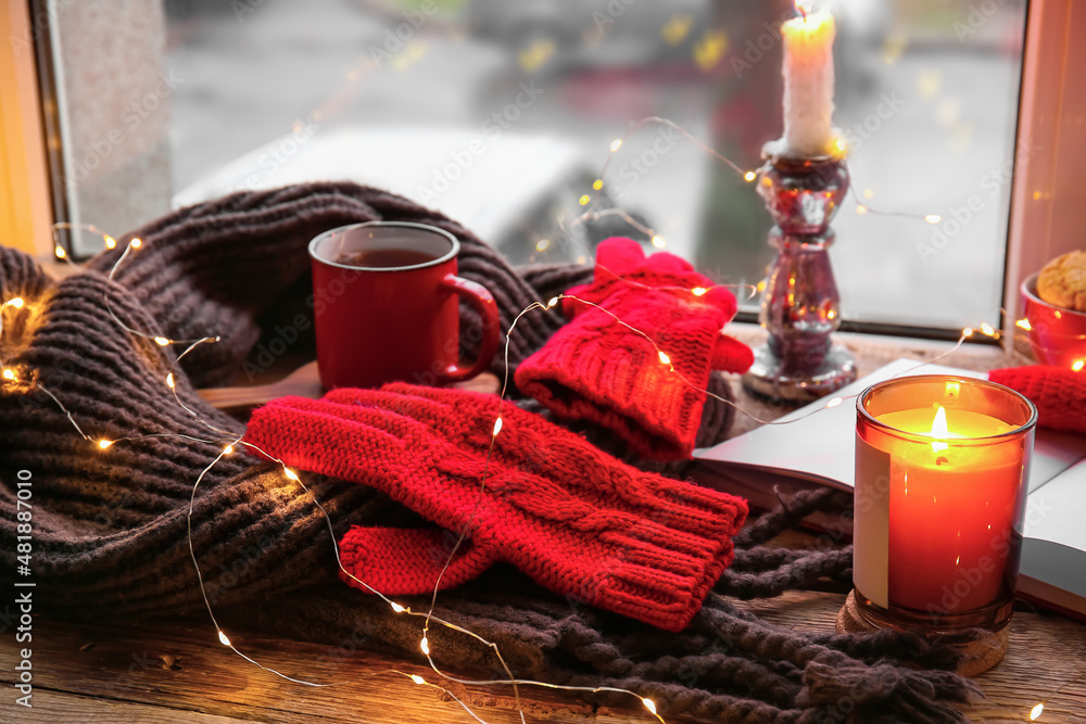 Warm gloves, scarf, Christmas lights and burning candle on windowsill