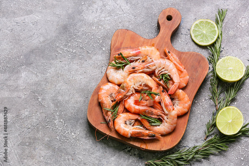 Wooden board of tasty shrimps with lemon on grey background