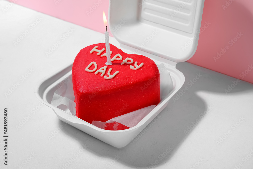 Plastic lunch box with tasty bento cake and burning candle on color background, closeup