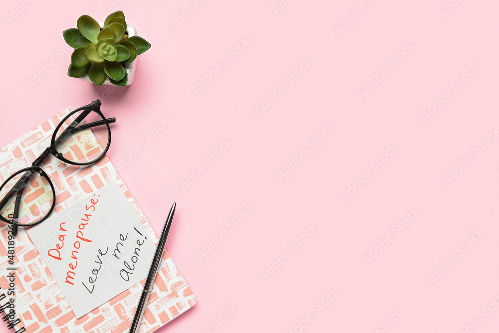 Notebook with text DEAR MENOPAUSE LEAVE ME ALONE, pen, eyeglasses and flowerpot on pink background