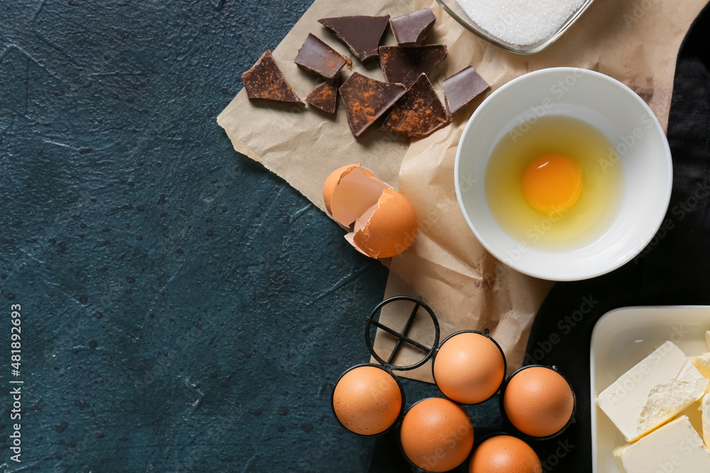 Bowl with fresh egg and ingredients for preparing chocolate brownie on black background