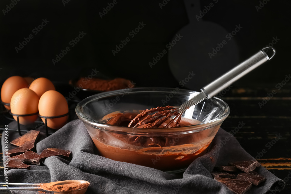 Bowl with fresh dough for preparing chocolate brownie on black background