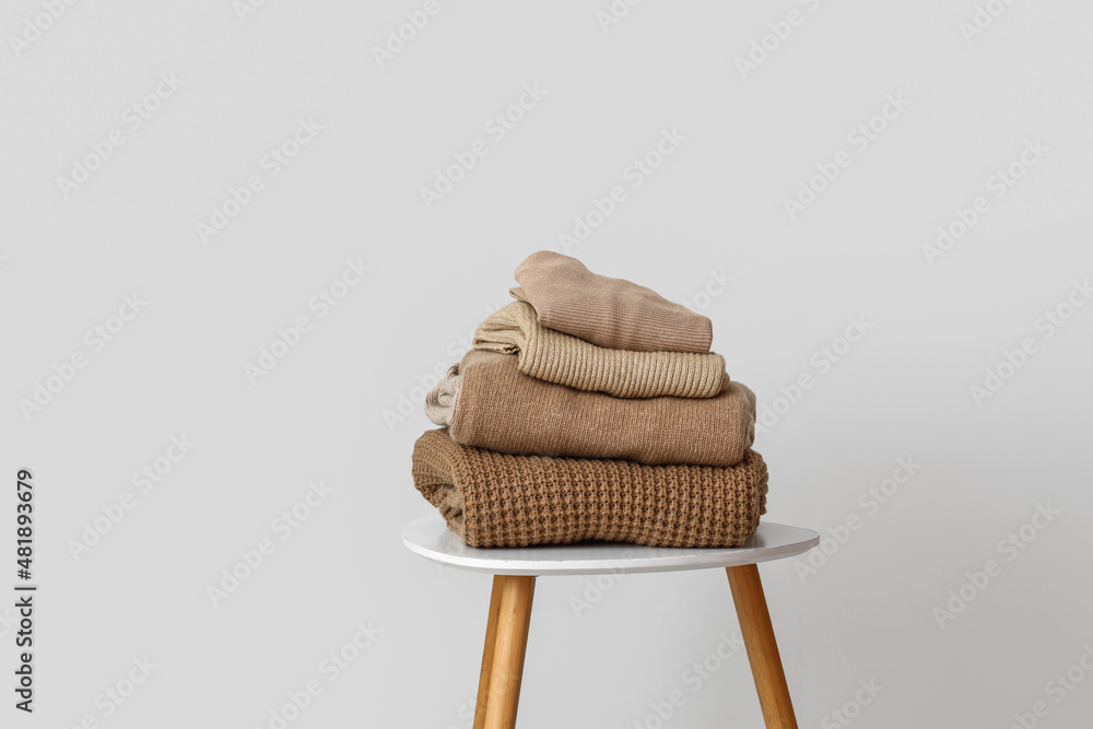 Stack of warm beige sweaters on table near light wall