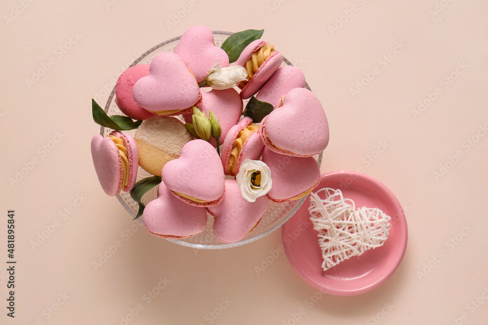 Dessert stand with tasty heart-shaped macaroons and flowers on beige background