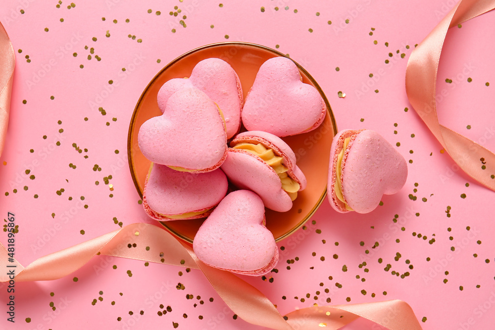 Plate with tasty heart-shaped macaroons and confetti on pink background