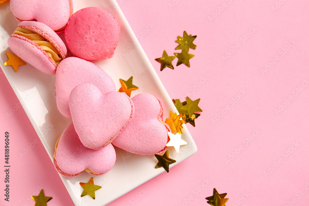 Plate with tasty heart-shaped macaroons and confetti on pink background