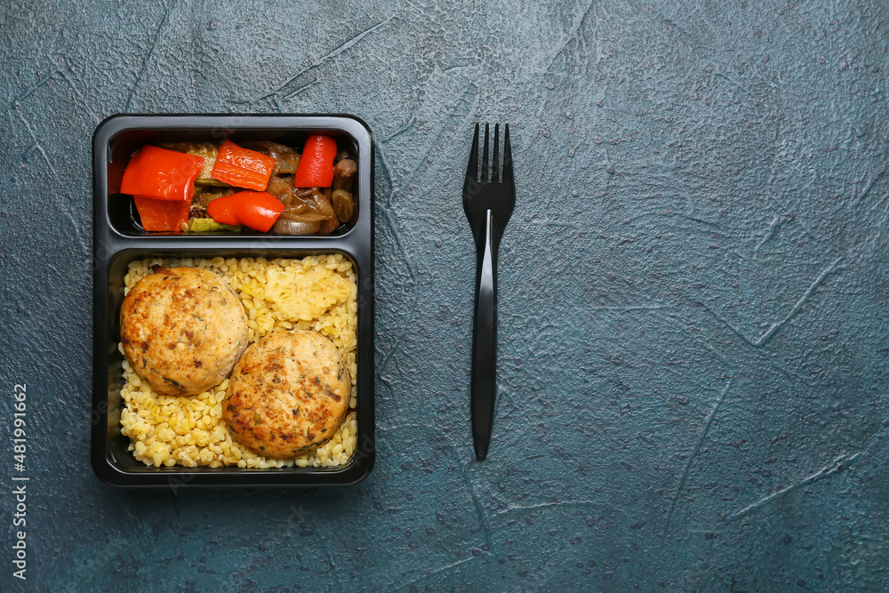 Food delivery container with delicious pearl barley, cutlets and vegetables on dark background