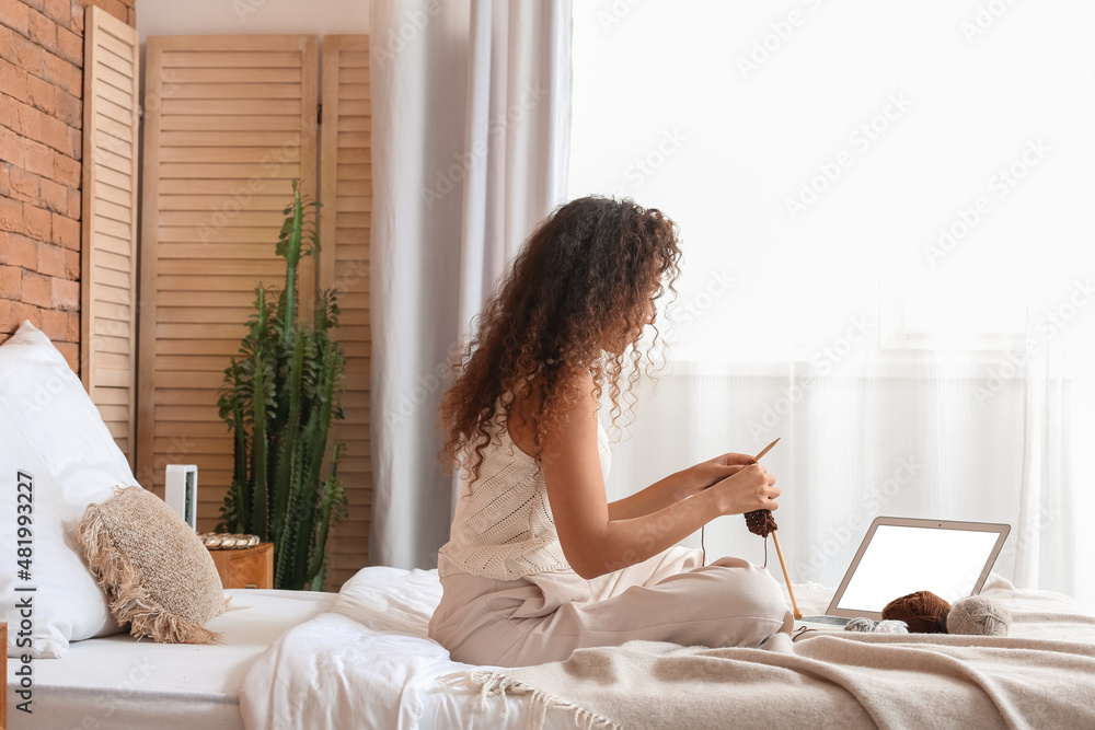 Young African-American woman taking online knitting classes at home