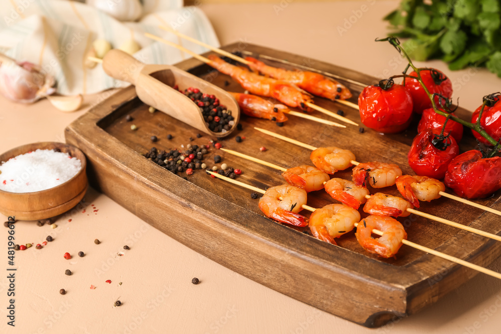 Wooden board with grilled shrimp skewers and tomatoes on beige background