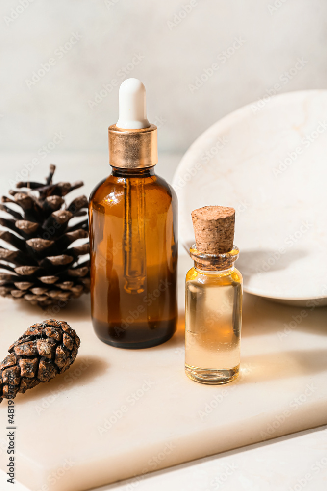 Board with bottles of essential oil and pine cones on light background, closeup