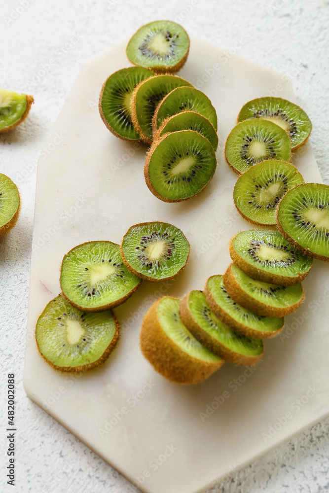 Board with slices of fresh kiwi on light background