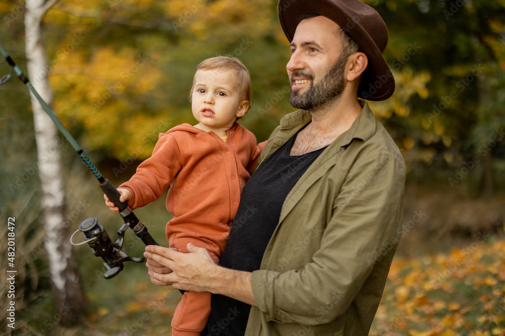 Smiling caucasian man fishing with little son on river or lake coast. Concept of leisure and weekend