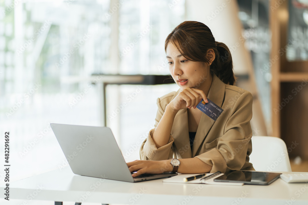 快乐的年轻漂亮女人在家用信用卡通过笔记本电脑在线购物