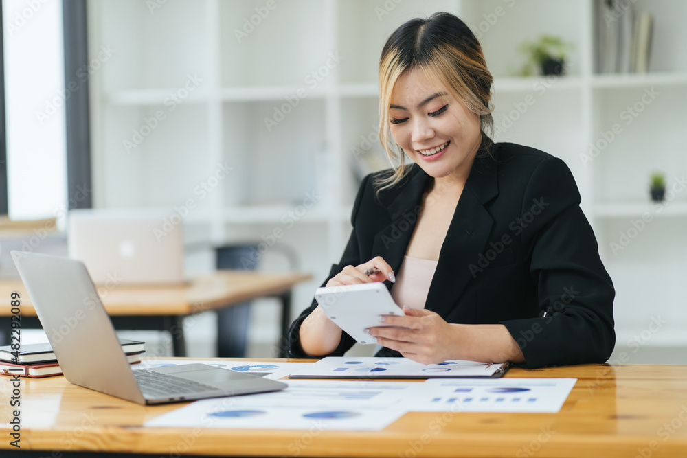 Young Asian woman entrepreneur/ Business owner using a smartphone and working with computer at home