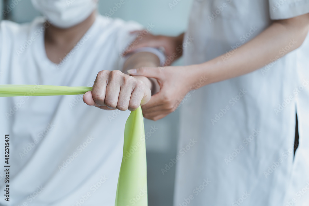 Asian physical therapist stretching athlete male patient shoulder and arm in clinic