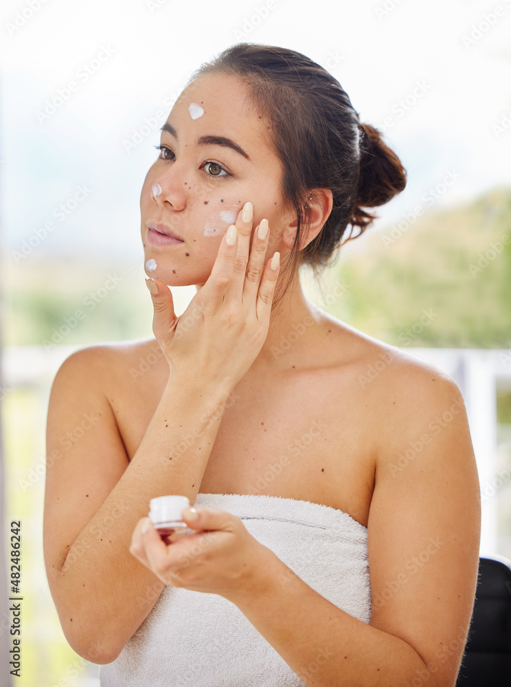 Keeping my face moisturised all day. Shot of a young woman applying moisturiser to her face during h