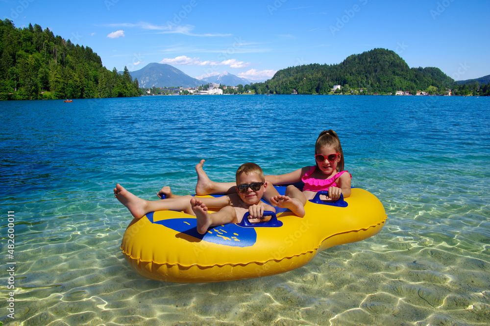 Boy and girl on inflatable float in lake. Little children floating in yellow raft on surface water.