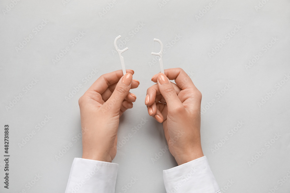 Woman with floss toothpicks on light background