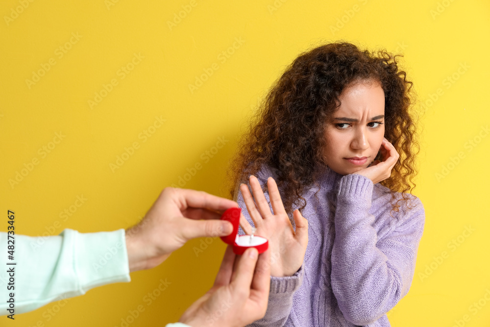 Young African-American woman rejecting marriage proposal on color background