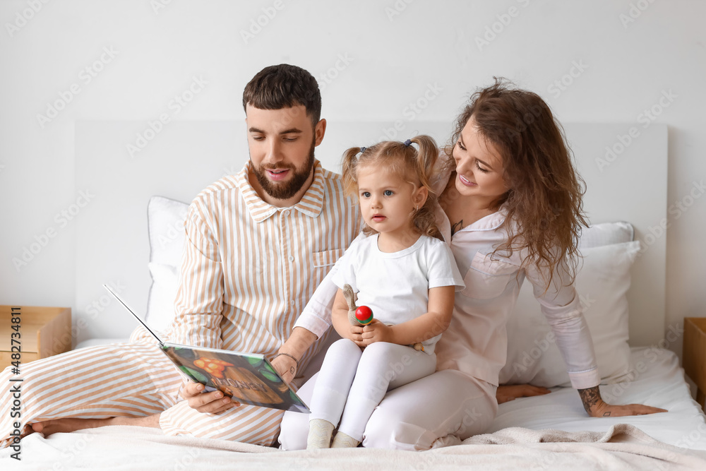 Happy young family reading book in bedroom at home