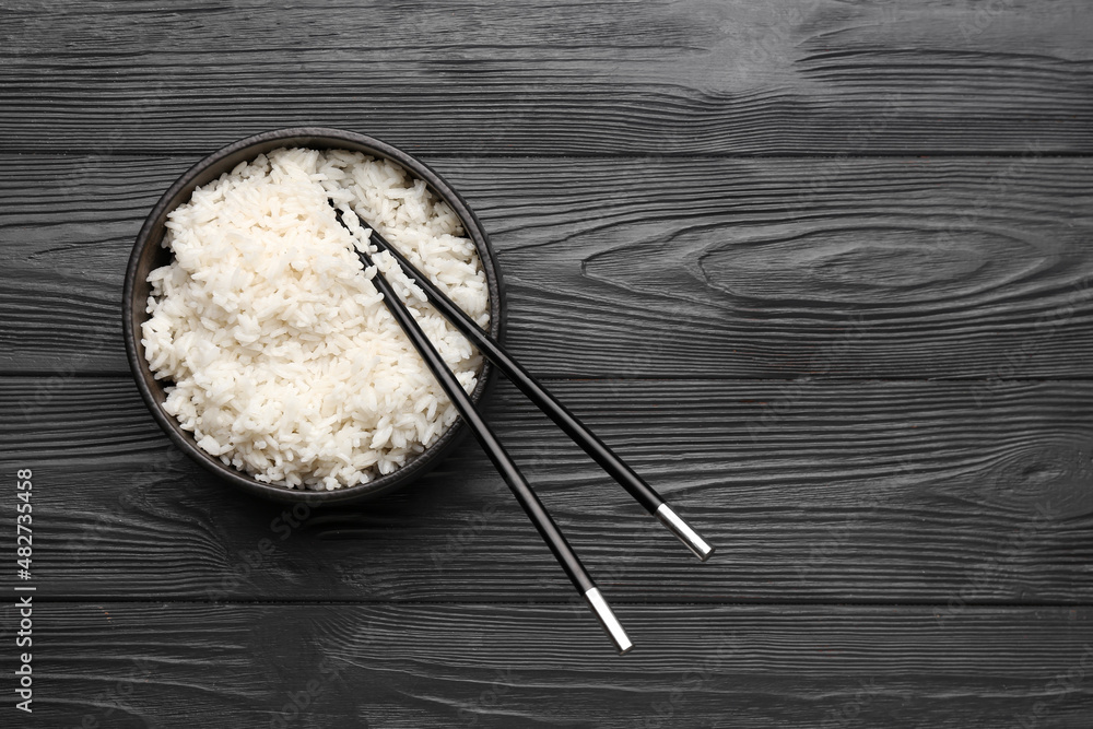 Bowl with tasty boiled rice and chopsticks on dark wooden background