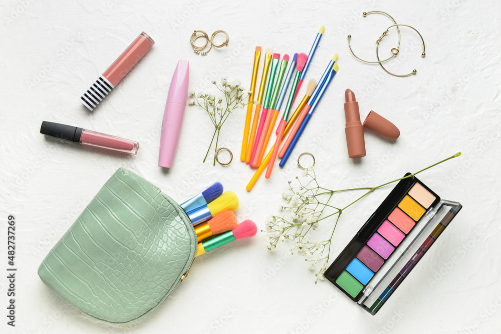 Bag with makeup brushes and cosmetic products on light background