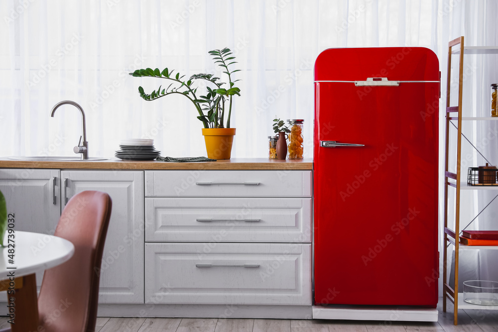 Stylish red refrigerator, counter and houseplant in kitchen