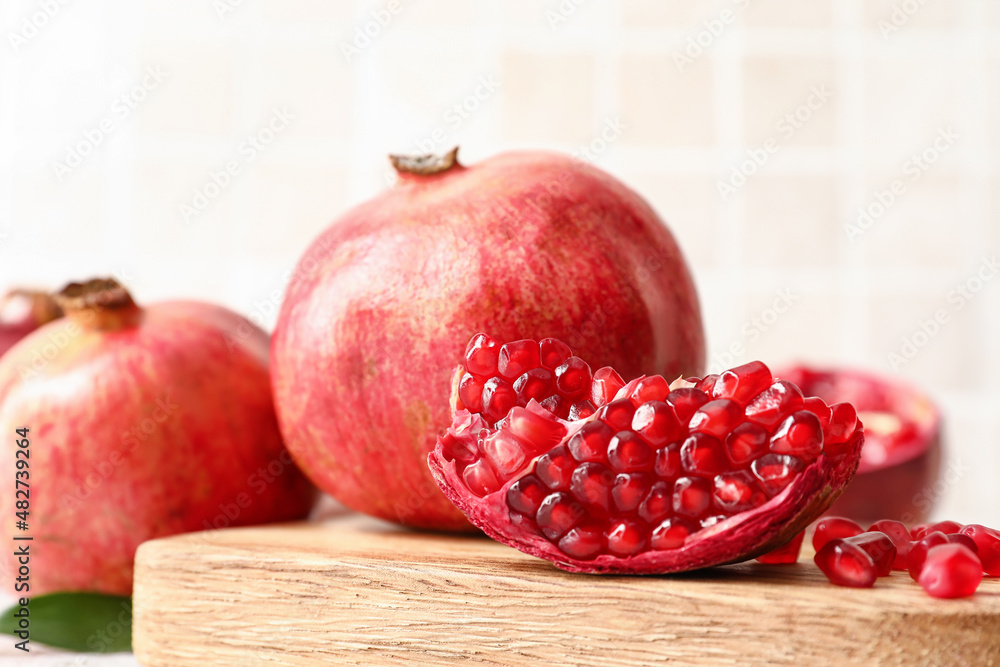 Board with ripe tasty pomegranate piece on light background, closeup