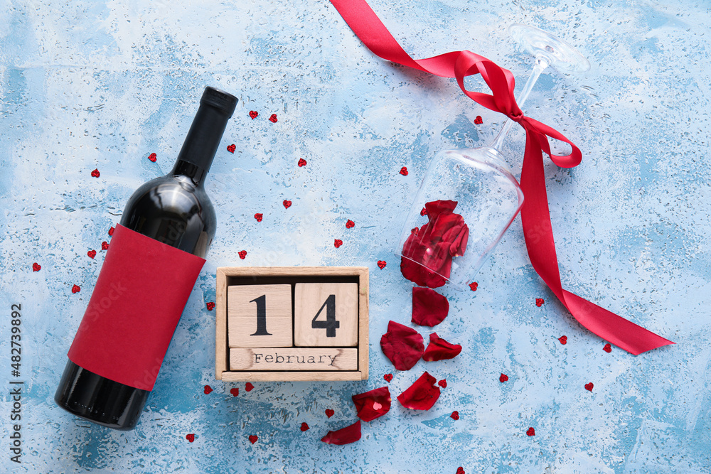 Calendar with date of Valentines Day, glass, wine bottle and rose petals on blue background