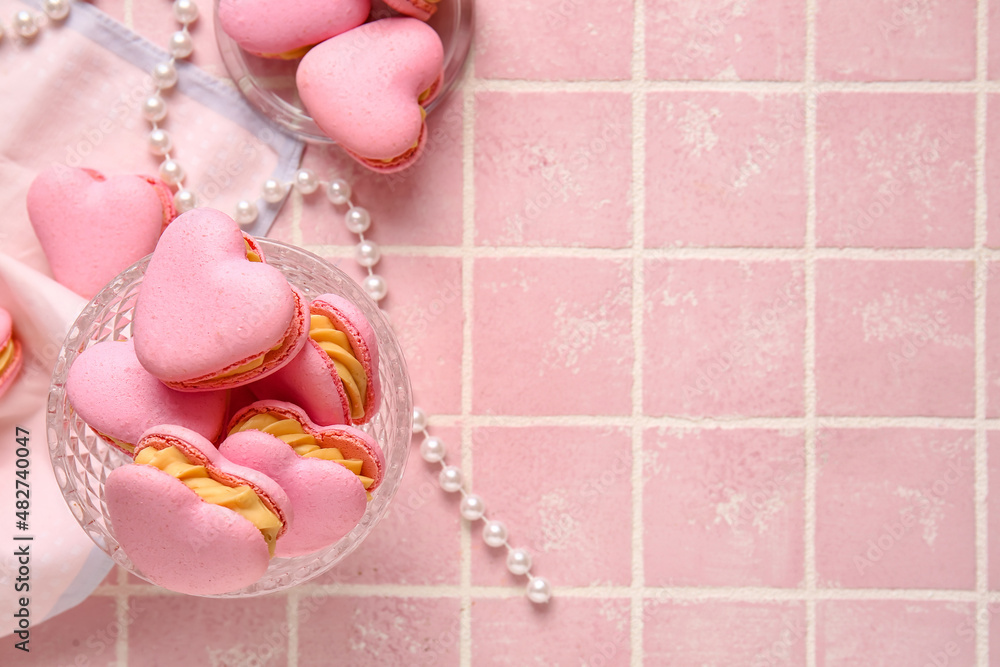 Dessert bowl with tasty heart-shaped macaroons on pink background