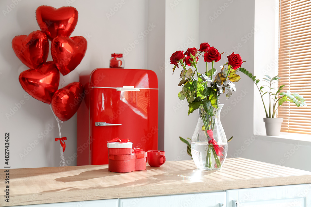 Vase with roses, cup and gift boxes on counter in room decorated for Valentines Day celebration