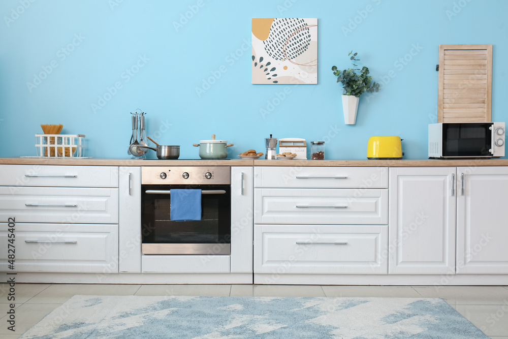 Modern kitchen with white counters and utensils near color wall