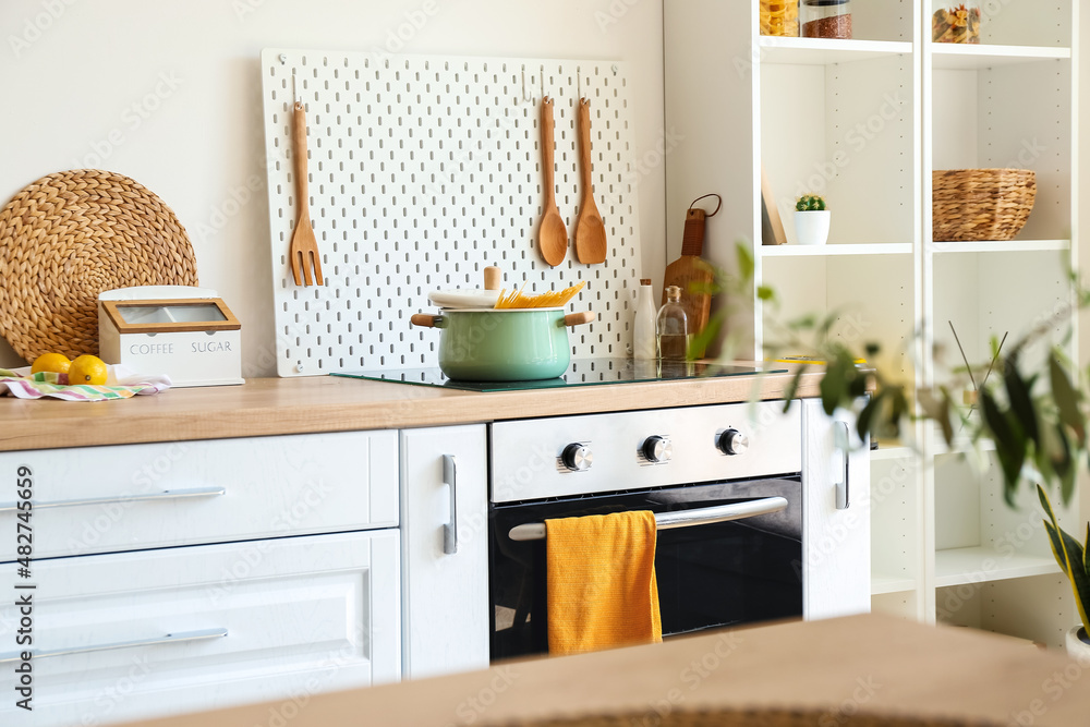 Cooking pot on stove and peg board with wooden spatulas in kitchen