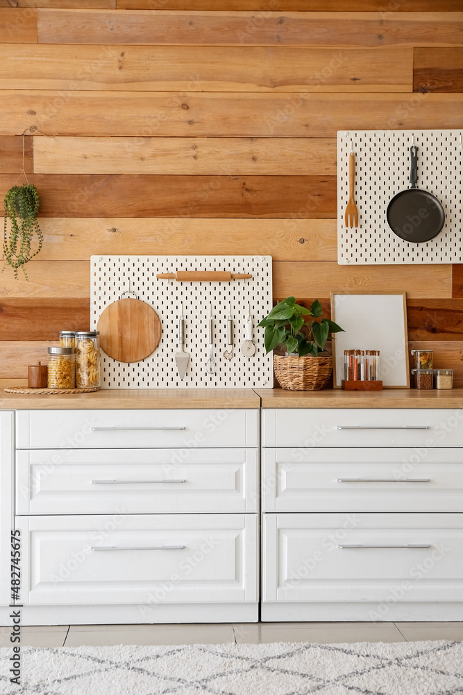 Interior of modern kitchen with white counters, peg boards and wooden wall