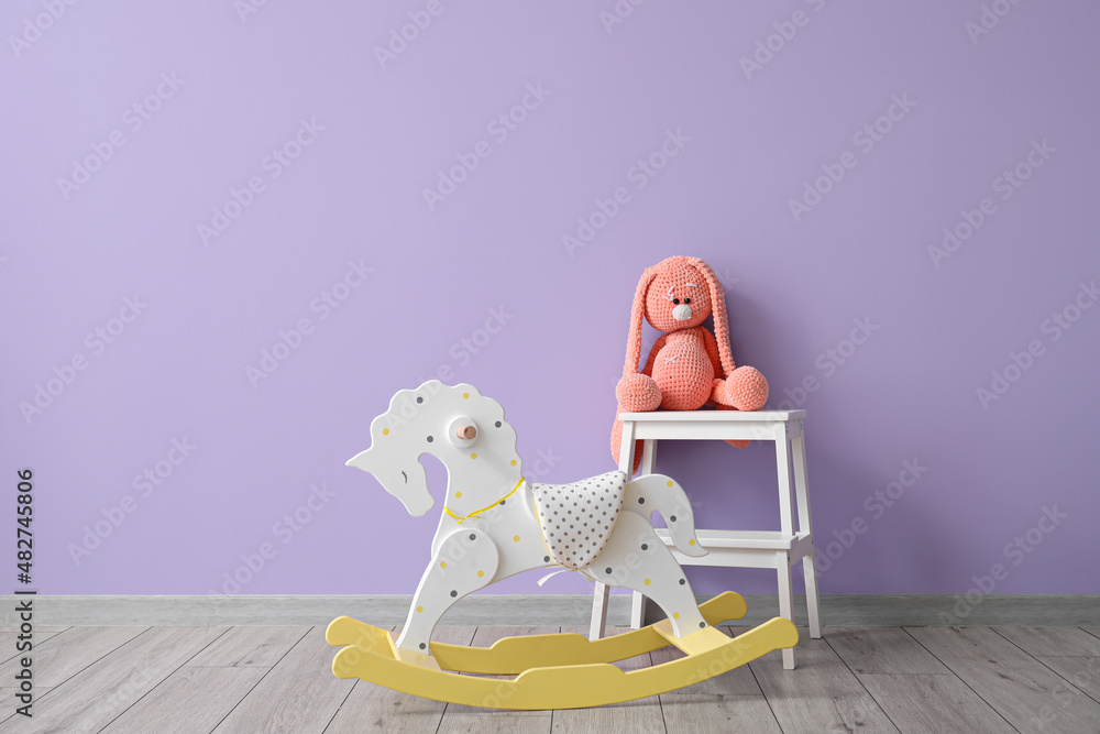 Rocking horse and stepladder stool with toy rabbit near color wall